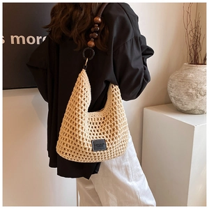 Détail d'un sac hobo en paille tressée beige orné de perles décoratives en bois marron