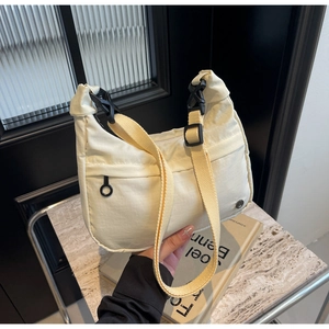 Détail du sac bandoulière en nylon crème avec sangle jaune et boucle en plastique