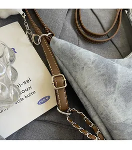 Detail of gray washed denim tote bag with brown leather and silver metal chain strap
