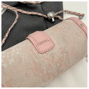Detail of pink cylindrical crossbody bag featuring jacquard floral fabric and gold chain strap