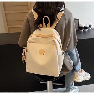 Detailed back view of a cream lightweight nylon backpack worn by a model in a cafe setting