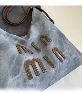 Detail of light blue washed tote bag featuring leather letter patch and slim shoulder strap
