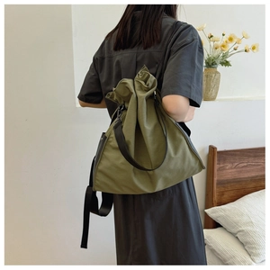 Army green canvas bucket bag with drawstring closure and black leather strap worn by a model