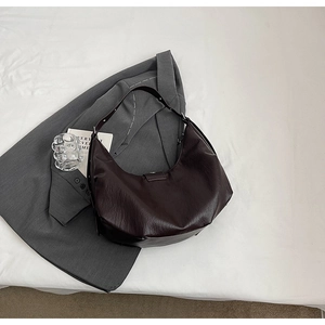 Vue à plat d'un sac hobo en similicuir marron foncé sur tissu blanc avec décor