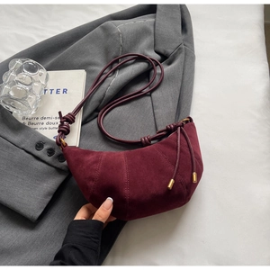 Detail of burgundy suede crescent bag resting on grey blazer with minimalist strap
