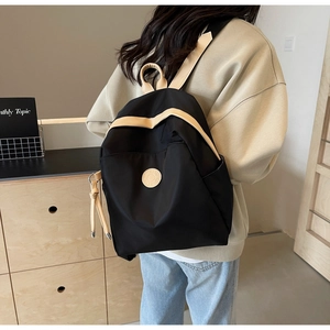 Side view of black nylon backpack with beige trim details shown in a modern home setting