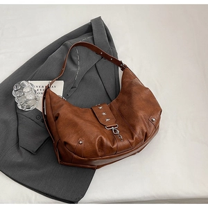 Détail d'un sac hobo marron avec clous étoiles argentés et fermoir rotatif sur blazer