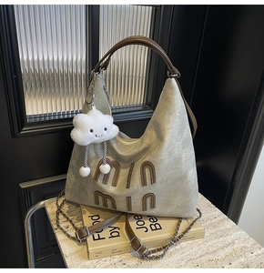 Detail of grey-green canvas hobo bag with leather letters and fluffy cloud charm