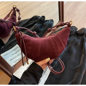 Detail of burgundy suede crescent bag with signature knotted strap and metallic tips