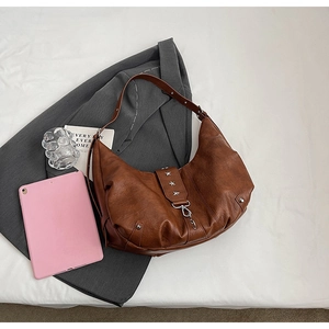 Détail d'un sac demi-lune en similicuir marron avec rivets étoiles et chaîne sur costume