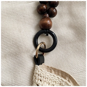 Détail de la bandoulière en perles de bois et anneau doré sur un sac cabas tressé