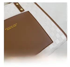 Close-up of white checkerboard tote bag featuring brown leather pocket and gold metal rivets