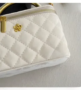 Detail of white quilted handbag with gold circular handle and camellia flower charm