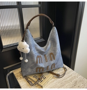 Detail of light blue denim tote with brown leather letters and white plush cloud charm