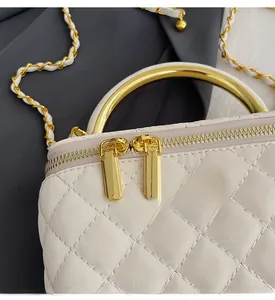 Detail of white quilted handbag showing gold metal chain strap and decorative floral zipper