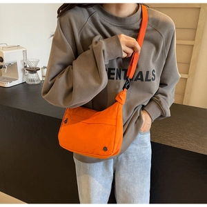 Détail d'un sac bandoulière orange vif avec poche zippée et sangle réglable sur modèle