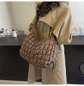 Rear view of model wearing a large dark brown quilted puffer shoulder bag with trench coat