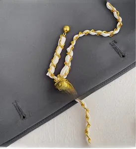 Detail of golden metal chain strap with adjustable gold ball buckle and white leather