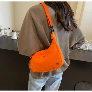 Détail du sac dumpling en nylon orange vif avec bandoulière réglable porté par un mannequin