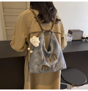 Detail view of denim tote bag with brown leather trim and fluffy cloud charm accessory