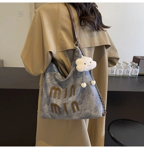 Close-up of a grey washed denim tote bag with leather straps and a plush cloud charm