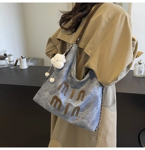 Detail of light blue washed canvas tote with brown leather strap and plush cloud charm