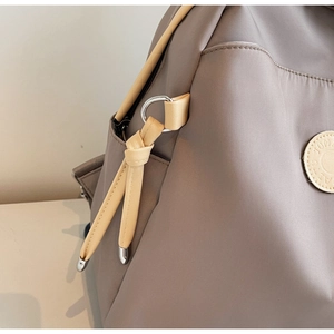 Detail view of khaki nylon fabric with leather trim and metal hardware on a women's backpack