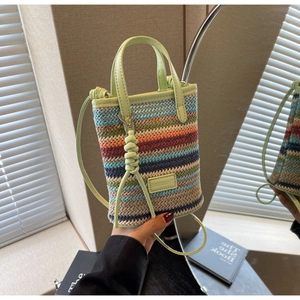 Detail of colorful hand-woven straw crossbody bag with green leather handles and brand plaque