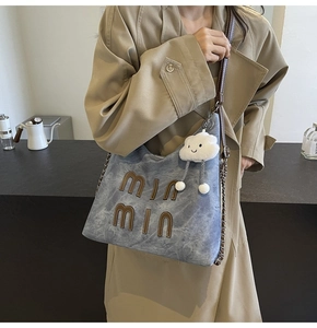 Detail of blue canvas tote bag with brown leather letters and cloud plush charm