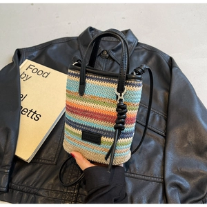 Detail of colorful striped woven beach bag with black leather handles and logo plate