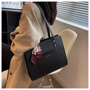 Detail of black tote bag with floral scarf and gold logo on textured leather surface