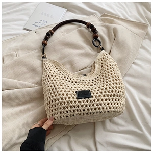 Detail of woven tote bag with wooden bead handle and logo patch on beige fabric