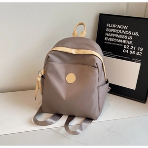 Close-up of taupe nylon backpack showing side pockets and premium leather circular patch