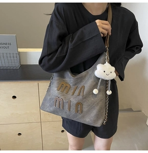 Detail view of dark grey tote with brown min letters and white cloud plush charm