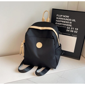Detail view of the black nylon commuter backpack with beige handles and front zip pocket