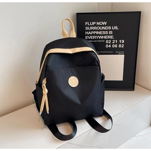 Detail of black nylon backpack featuring beige handles and a front zipper pocket