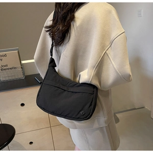 Détail du sac bandoulière en nylon noir avec une sangle réglable et un logo en métal
