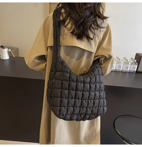 Detail of a large black quilted cloud bag worn with a classic beige trench coat in a cafe