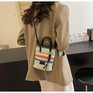 Colorful striped straw bucket bag with black handles shown on a model in a cafe setting
