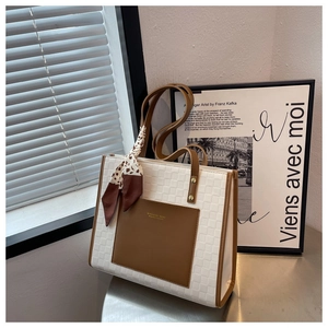 Close-up of beige woven tote bag with brown leather pocket and floral silk scarf detail