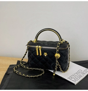 Detail view of black quilted vanity bag with golden camellia and chain strap