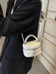 Mini white quilted crossbody bag with silver chain strap and top handle displayed by model