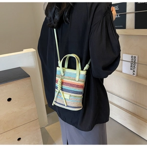 Detail of colorful striped woven straw crossbody bag with leather strap on a model
