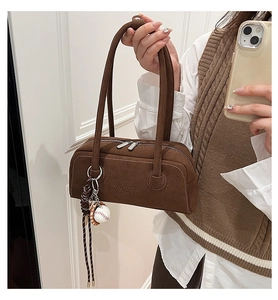 Detail of a brown faux suede shoulder bag featuring silver zippers and a baseball pendant
