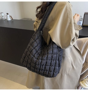 Detail of a large black quilted puffy shoulder bag with glossy nylon texture shown on model