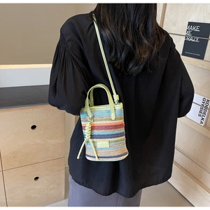Detail of colorful striped straw bucket bag showing woven texture and green leather strap