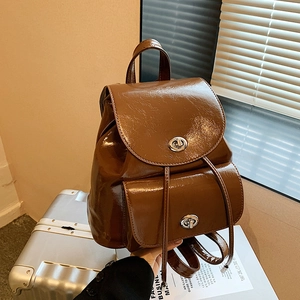 Detail of a brown glossy leather backpack with silver metal twist locks and drawstrings
