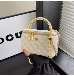 Detail of a quilted cream mini vanity bag featuring a gold handle and camellia charm