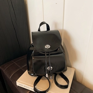 Detail of glossy black leather backpack with flap lock, drawstring, and shiny finish texture
