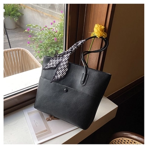 Detail of black pebbled leather tote bag with geometric print silk scarf handle on windowsill